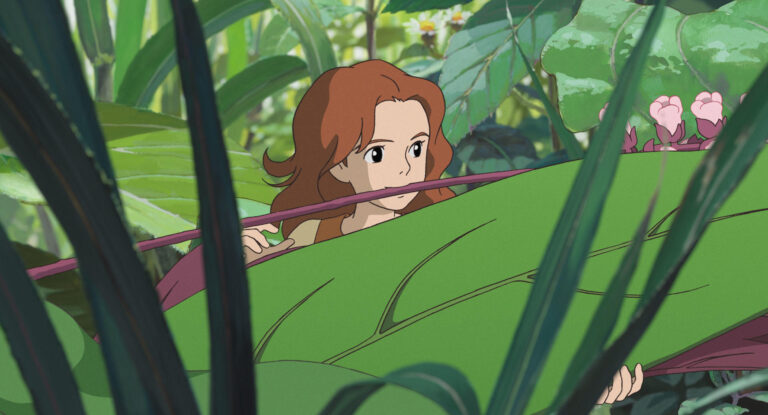 Arrietty looking through large leaves in the garden in an official film still