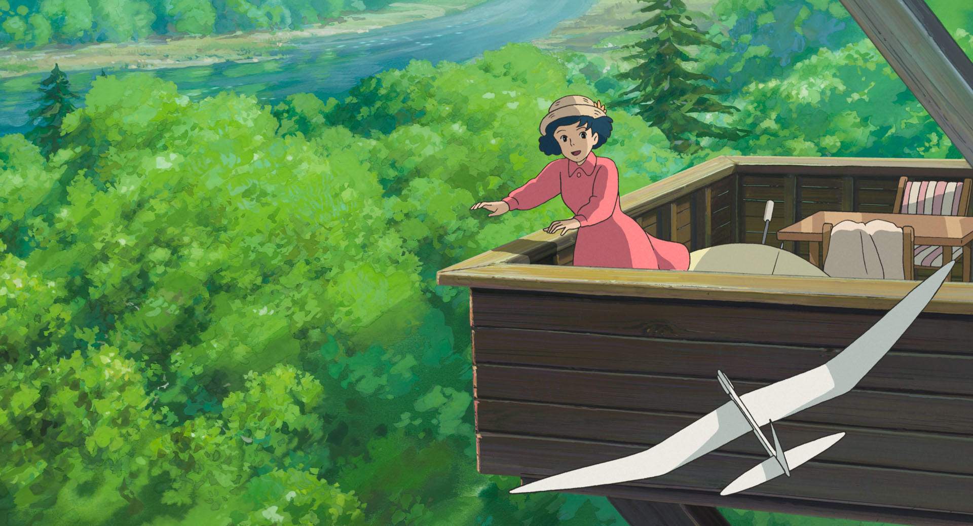 A woman in red outdoors as a paper airplane passes overhead in an official still from The Wind Rises